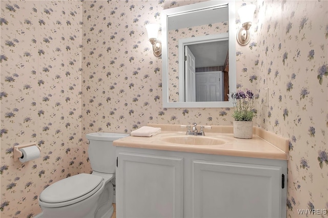 bathroom with toilet, wallpapered walls, and vanity