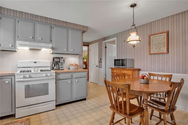 kitchen with white gas stove, stainless steel microwave, wallpapered walls, and under cabinet range hood