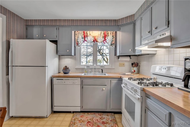 kitchen featuring wallpapered walls, under cabinet range hood, gray cabinets, white appliances, and a sink