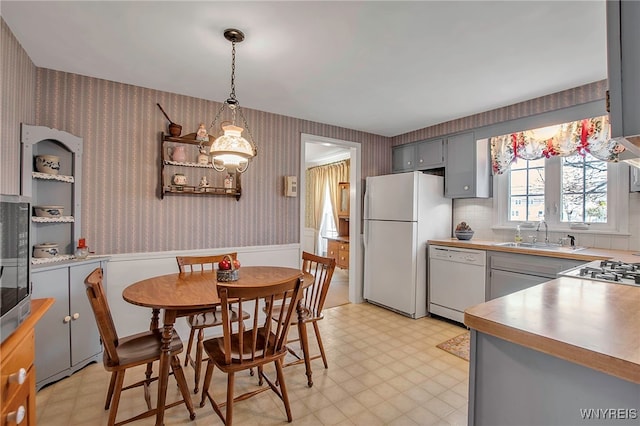 kitchen with white appliances, light floors, wallpapered walls, a sink, and hanging light fixtures