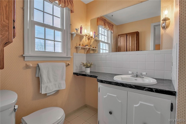 half bath featuring tile patterned floors, toilet, vanity, and wallpapered walls