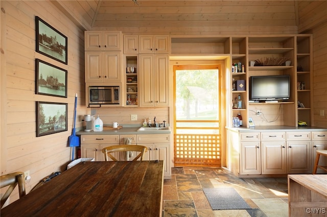 kitchen featuring open shelves, stainless steel microwave, a sink, stone tile floors, and wooden walls