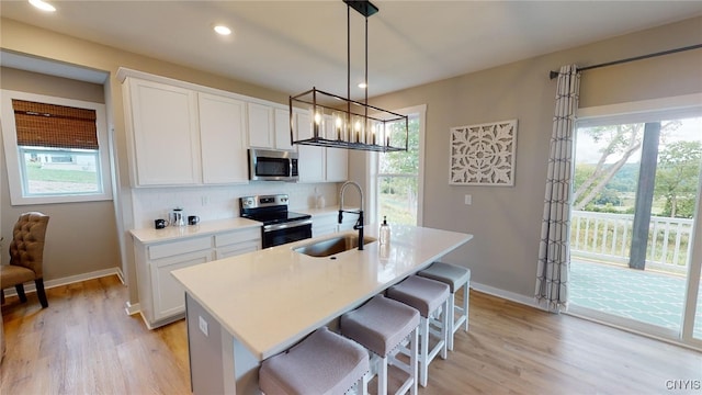 kitchen with a kitchen island with sink, a sink, decorative backsplash, appliances with stainless steel finishes, and white cabinetry