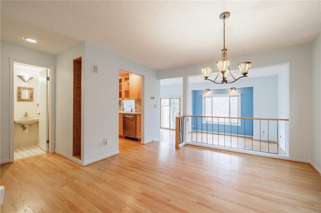 unfurnished dining area with visible vents, baseboards, a sink, a notable chandelier, and light wood-type flooring