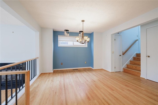 spare room featuring baseboards, a chandelier, stairway, light wood-type flooring, and a textured ceiling