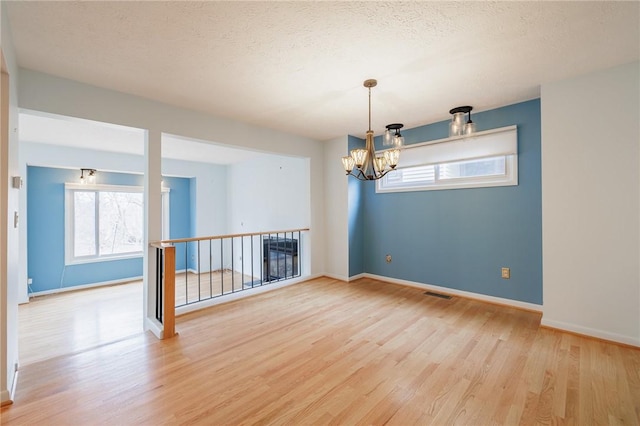 unfurnished room with an inviting chandelier, a textured ceiling, baseboards, and light wood-style floors