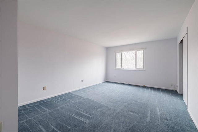 unfurnished room with baseboards and dark colored carpet