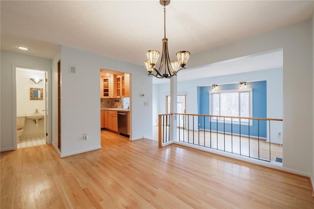 unfurnished dining area with light wood finished floors, visible vents, baseboards, a notable chandelier, and a sink