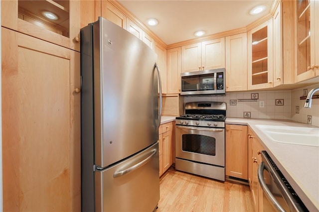 kitchen with a sink, stainless steel appliances, light countertops, light wood-style floors, and tasteful backsplash