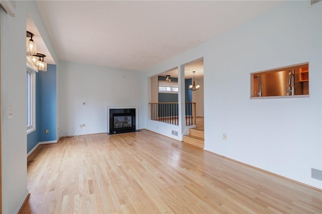 unfurnished living room with stairway, wood finished floors, visible vents, an inviting chandelier, and a fireplace with flush hearth