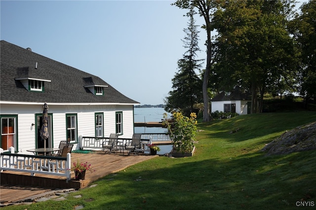 exterior space with a deck with water view, a lawn, and a shingled roof