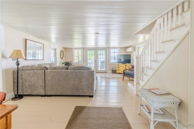 living room featuring stairway, baseboards, french doors, light wood-style floors, and a wall mounted air conditioner