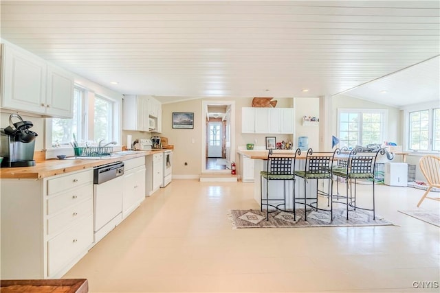 kitchen featuring wooden counters, a kitchen bar, lofted ceiling, white cabinets, and white appliances