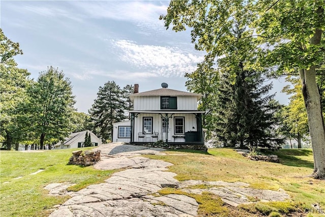 view of front of home featuring board and batten siding, a front lawn, a porch, and a chimney