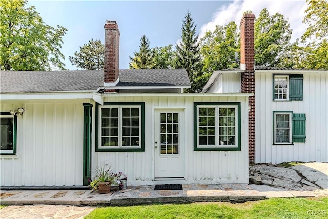 back of house with a shingled roof, board and batten siding, and a chimney