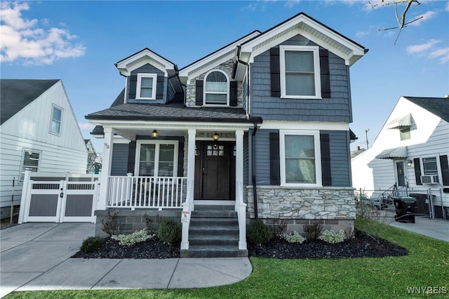 view of front of house with a gate, fence, a porch, concrete driveway, and stone siding