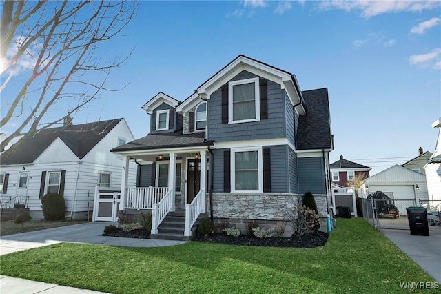 view of front of house featuring a front lawn, a gate, stone siding, fence, and covered porch