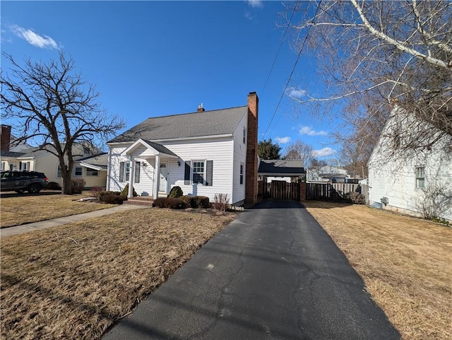 bungalow-style house with driveway, a front lawn, a chimney, and fence