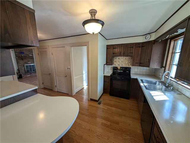 kitchen featuring light wood-type flooring, light countertops, decorative backsplash, black appliances, and a sink