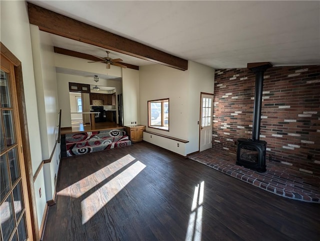 living room featuring a ceiling fan, wood finished floors, baseboards, a wood stove, and vaulted ceiling with beams