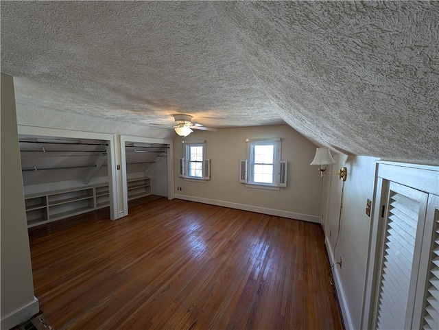 bonus room featuring a textured ceiling, wood finished floors, baseboards, ceiling fan, and vaulted ceiling