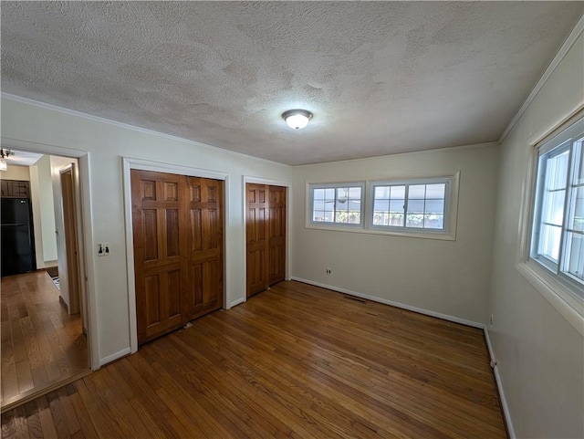 unfurnished bedroom featuring wood finished floors, baseboards, freestanding refrigerator, ornamental molding, and multiple closets