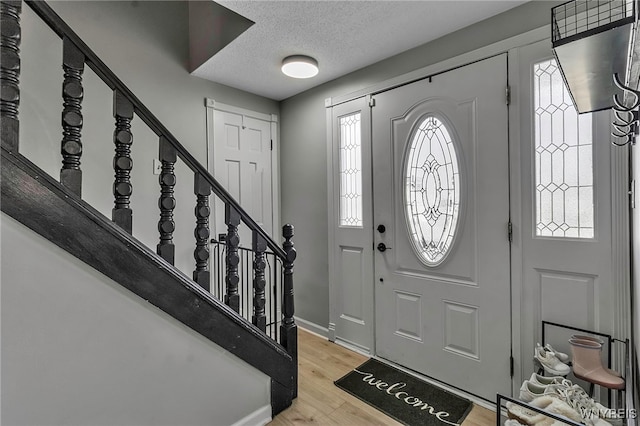 foyer with stairs, light wood-style floors, baseboards, and a textured ceiling