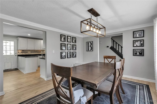 dining room with baseboards, stairway, ornamental molding, light wood-style floors, and a textured ceiling