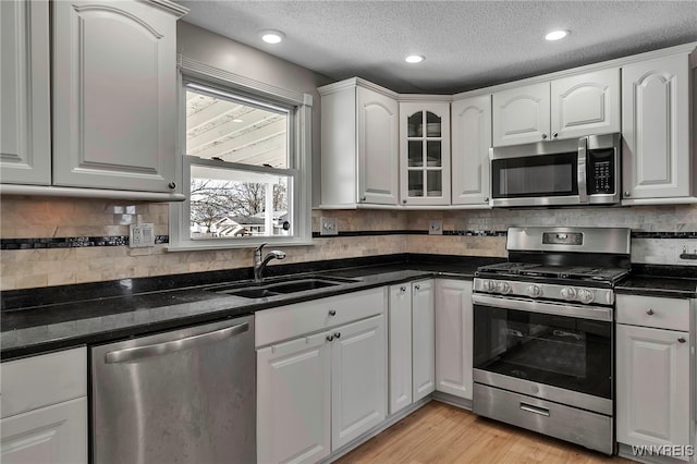 kitchen with light wood-style flooring, a sink, tasteful backsplash, white cabinetry, and appliances with stainless steel finishes