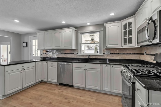 kitchen featuring light wood-style flooring, a sink, dark countertops, stainless steel appliances, and a peninsula