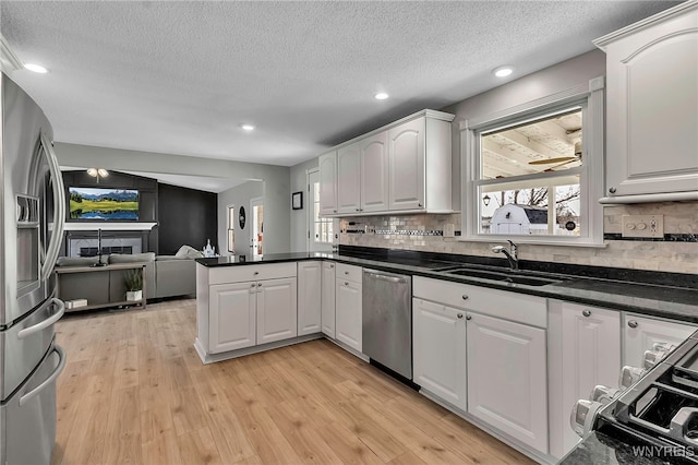 kitchen with light wood-type flooring, a sink, open floor plan, appliances with stainless steel finishes, and a peninsula