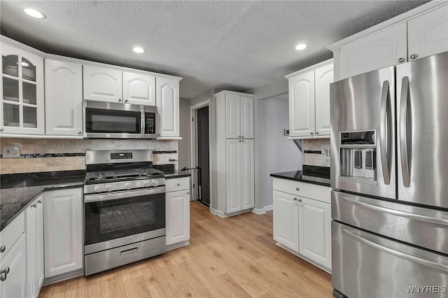 kitchen featuring tasteful backsplash, white cabinetry, light wood-style floors, appliances with stainless steel finishes, and glass insert cabinets