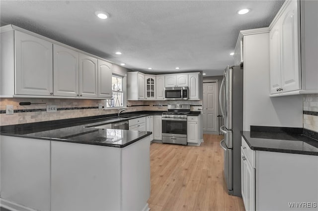 kitchen featuring stainless steel appliances, a peninsula, white cabinets, and light wood finished floors