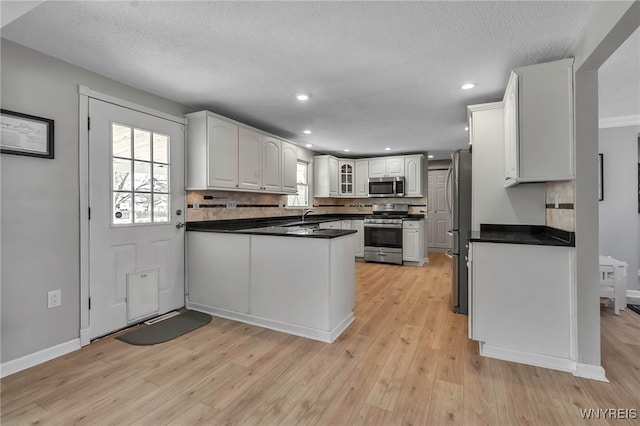 kitchen featuring appliances with stainless steel finishes, a peninsula, white cabinets, light wood finished floors, and glass insert cabinets