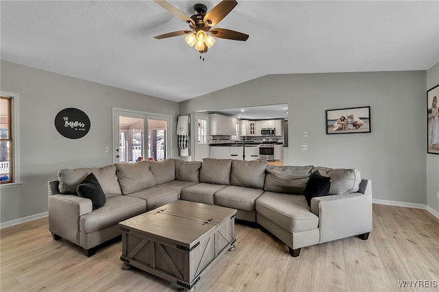 living area featuring light wood-style flooring, ceiling fan, baseboards, and vaulted ceiling