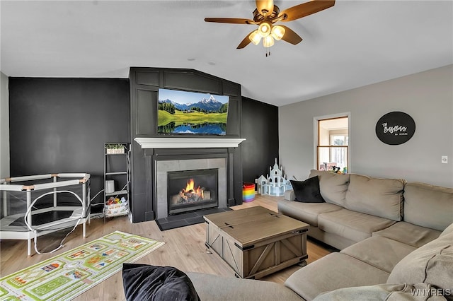 living area featuring a tiled fireplace, light wood-style flooring, a ceiling fan, and vaulted ceiling