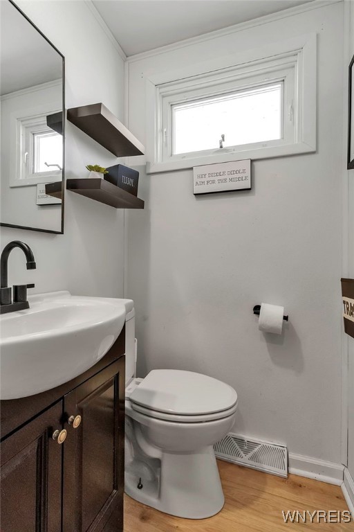 half bathroom with visible vents, crown molding, toilet, wood finished floors, and vanity