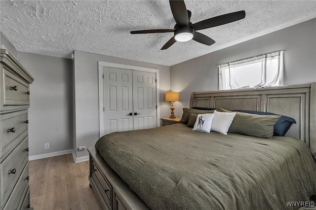 bedroom featuring light wood-style flooring, a ceiling fan, a textured ceiling, a closet, and baseboards