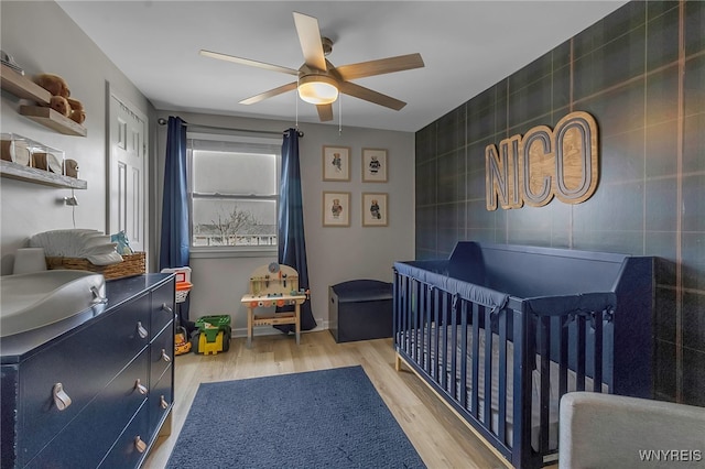 bedroom featuring tile walls, light wood-style flooring, baseboards, and ceiling fan