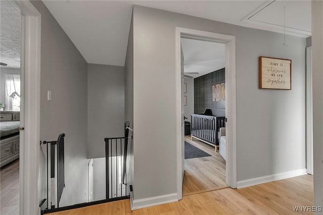 corridor with attic access, an upstairs landing, light wood-type flooring, and baseboards