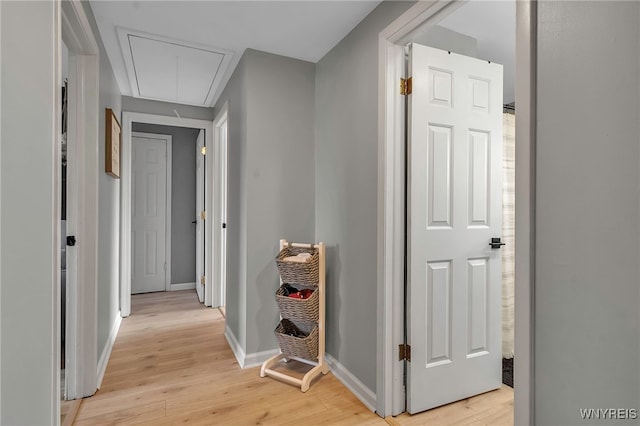 corridor with baseboards, attic access, and light wood-style floors