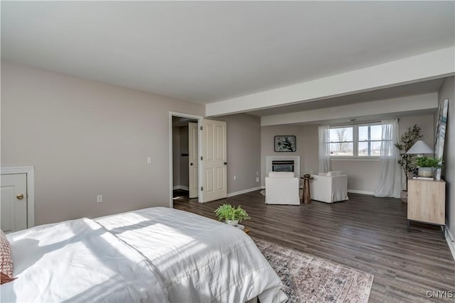 bedroom featuring a glass covered fireplace, baseboards, and wood finished floors