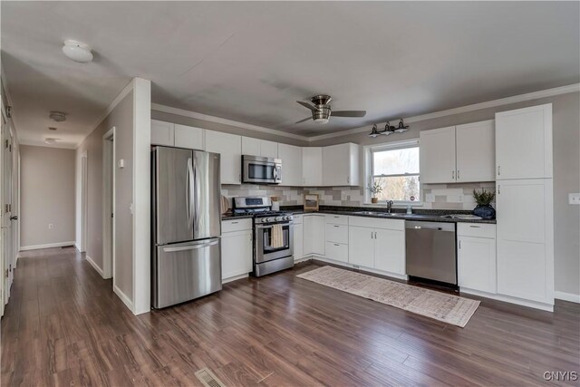 kitchen with dark countertops, dark wood finished floors, ornamental molding, stainless steel appliances, and a sink