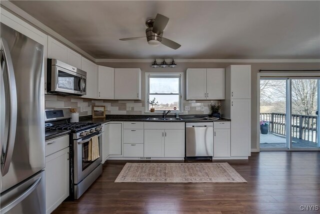 kitchen with dark countertops, ornamental molding, decorative backsplash, stainless steel appliances, and a sink