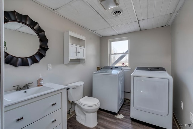 half bath with visible vents, toilet, wood finished floors, washer and dryer, and vanity