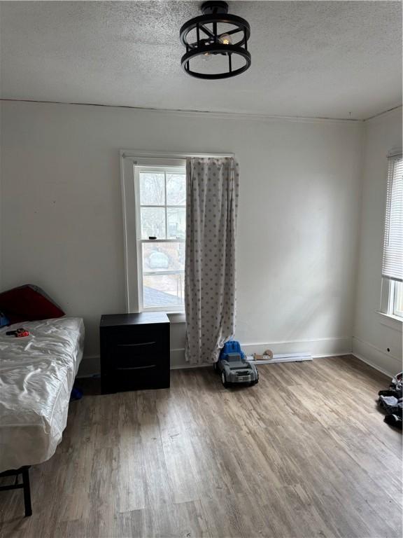 bedroom with multiple windows, a textured ceiling, baseboards, and wood finished floors