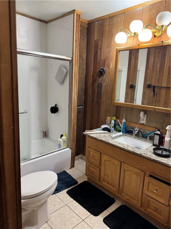 full bath featuring vanity, wooden walls, tile patterned flooring, toilet, and combined bath / shower with glass door