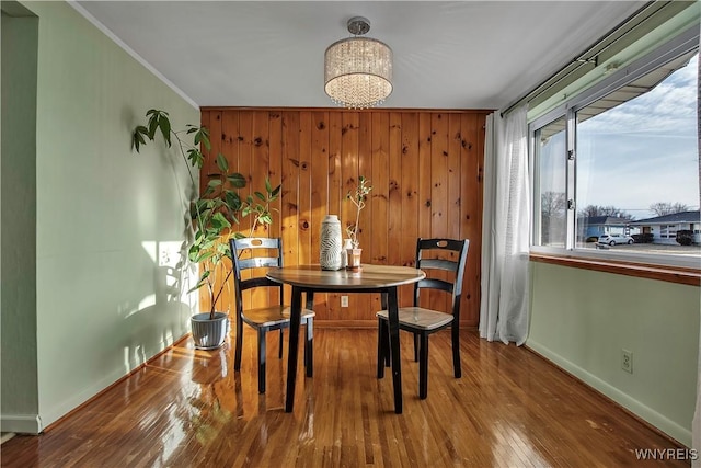 dining room featuring ornamental molding, hardwood / wood-style floors, wooden walls, an inviting chandelier, and baseboards