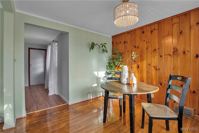 dining room with visible vents, wooden walls, ornamental molding, wood finished floors, and a notable chandelier