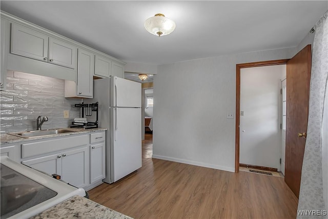 kitchen featuring light wood-type flooring, a sink, backsplash, white appliances, and baseboards